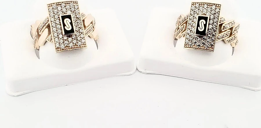 Two gold initial rings with pavé stones and a black onyx S panel on Cuban-link shanks