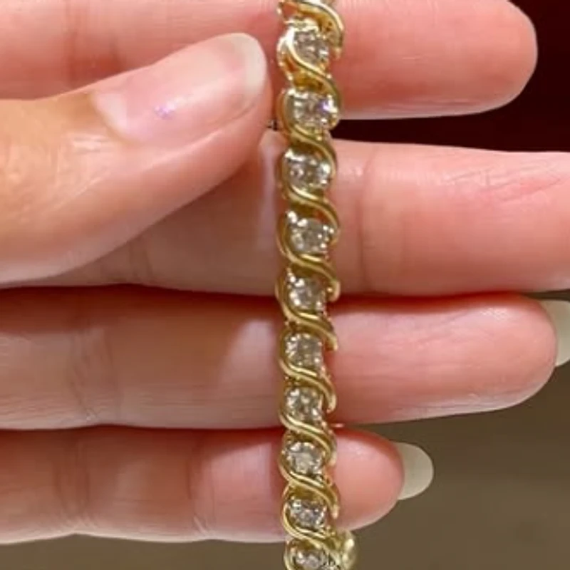Yellow gold swirl bracelet set with round diamonds held in a hand