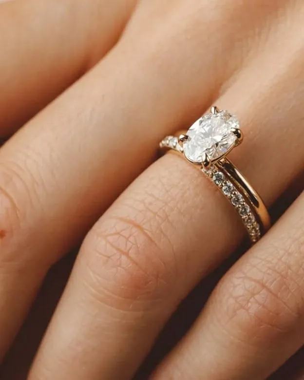 Hand wearing an oval diamond engagement ring with a matching diamond band