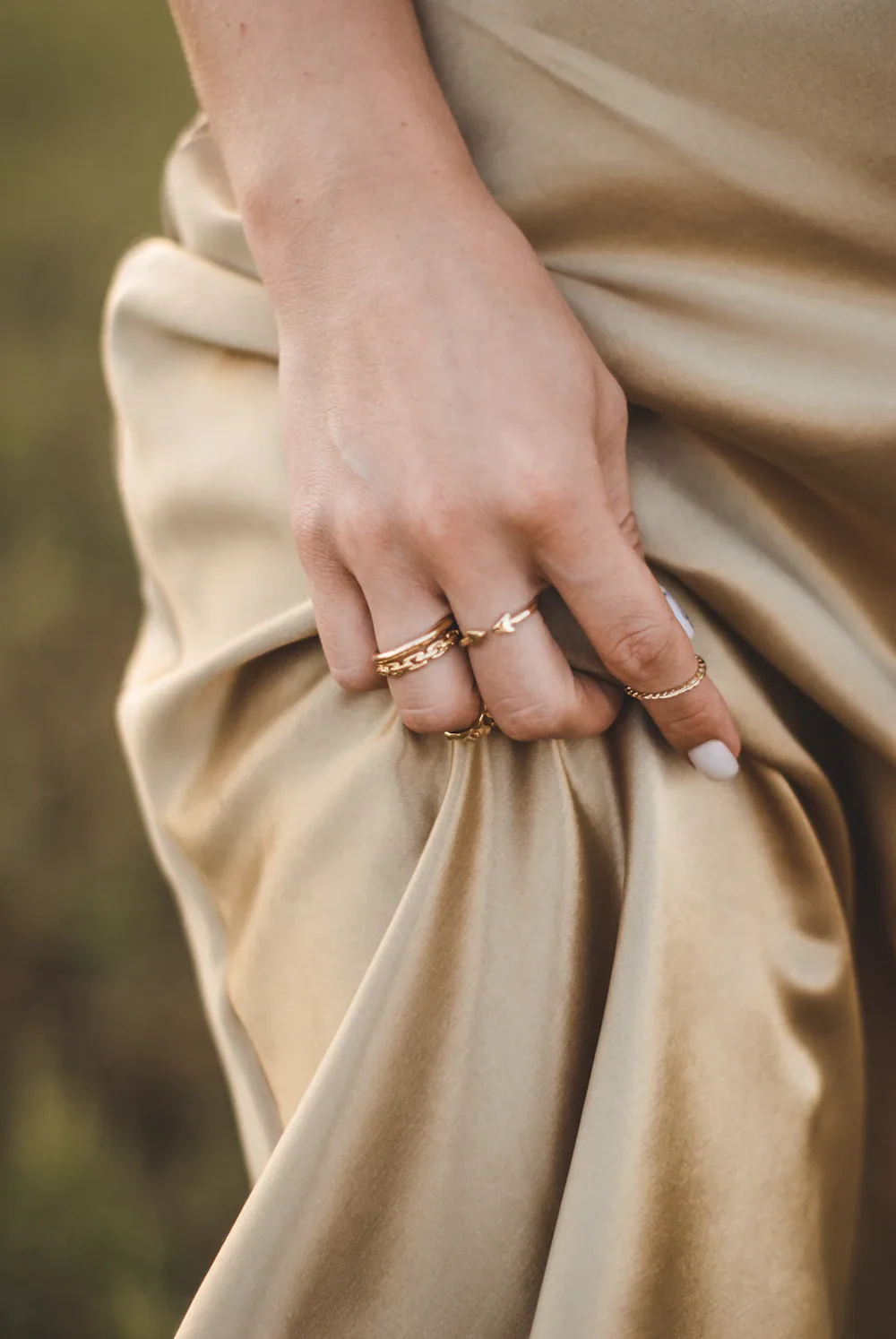 Hand wearing stacked gold rings against champagne satin