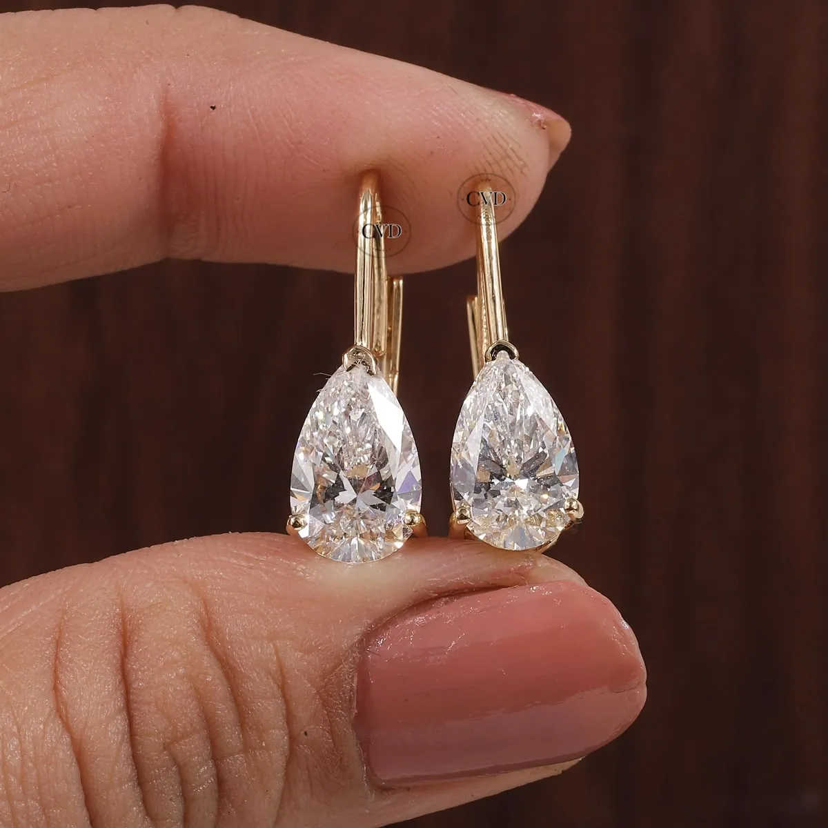 Pair of pear-shaped diamond drop earrings with gold hooks held between fingers