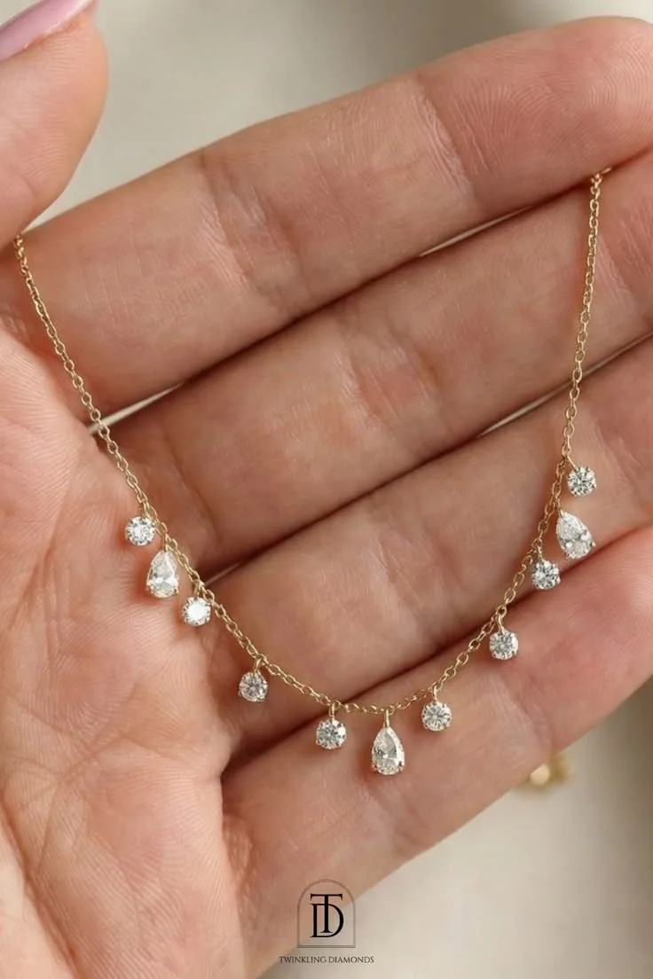 Gold necklace with round and pear-shaped diamond drops resting on a palm
