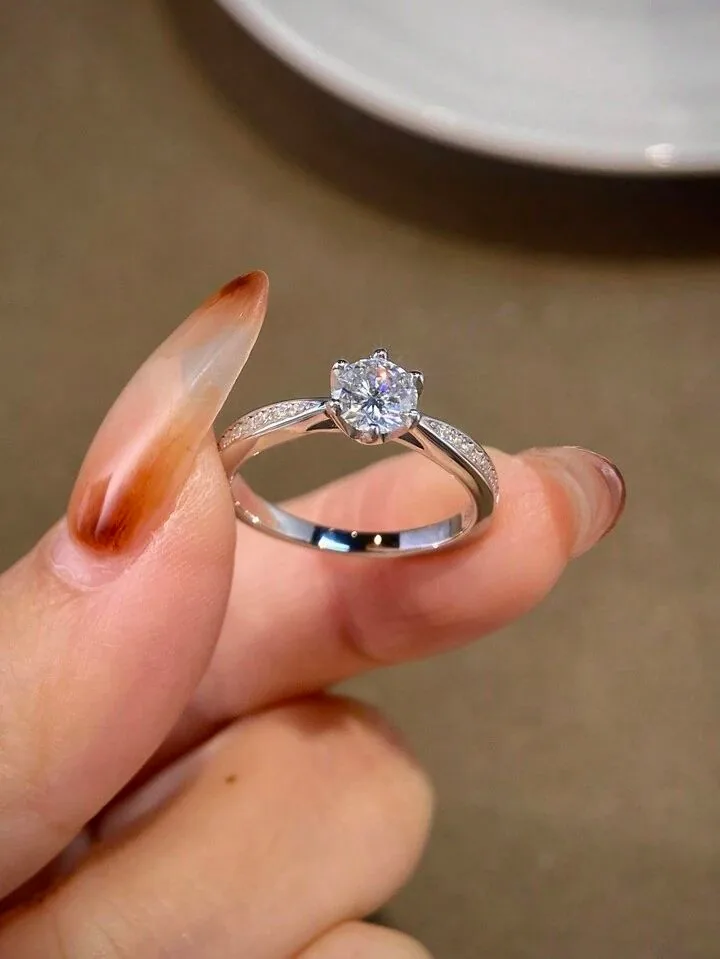 Hand holding a round diamond solitaire ring with diamond-set shoulders